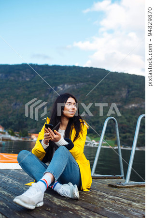 The girl tourist takes a photo on the phone by the lake in Norway. Young woman takes selfie. The girl tourist takes a photo on the phone by the lake in Norway. Young woman takes selfie. 94829870