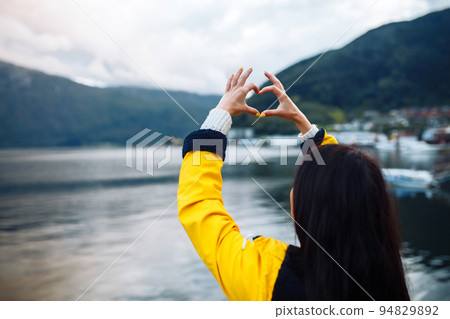 The girl tourist holding heart shaped hands and looking on the majestic mountains. 94829892