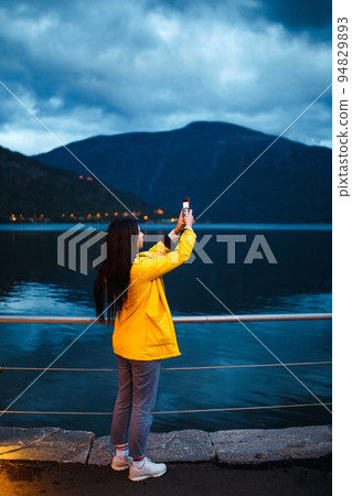 The girl tourist takes a photo on the phone by the lake in Norway. Active woman relaxing . 94829893