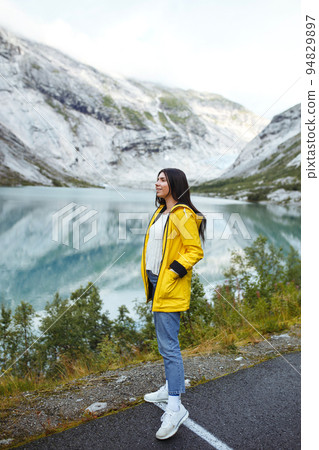 Girl tourist in yellow jacket posing on the lake in Norway. Active woman relaxing in the Norway. 94829897