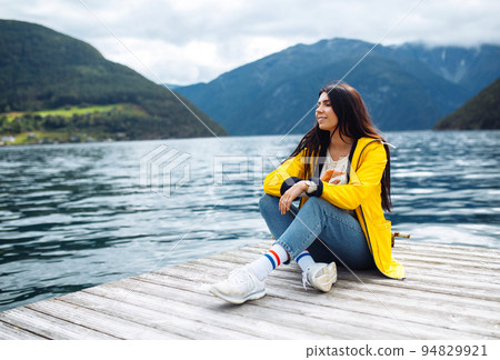 Girl tourist in yellow jacket posing on the lake in Norway. Active woman relaxing in the Norway. Girl tourist in yellow jacket posing on the lake in Norway. Active woman relaxing in the Norway. 94829921
