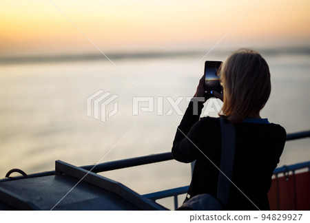 Girl tourist photographs a liner at sunset on the lake in Norway. Tourist takes sunset on the phone 94829927