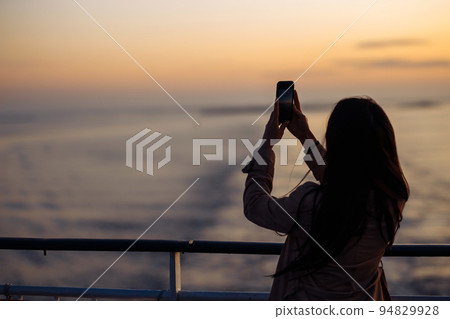 Girl tourist photographs a liner at sunset on the lake in Norway. Tourist takes sunset on the phone 94829928