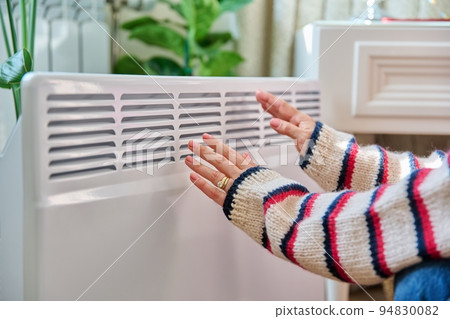 Close-up of woman hands warming near electric heating radiator 94830082