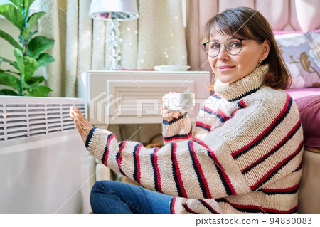 Woman warming herself in bedroom near electric heater Woman warming herself in bedroom near electric heater 94830083