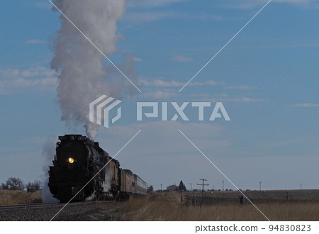 A legendary steam locomotive "Big Boy" that raises steam and white smoke and runs on the grasslands of the United States 94830823