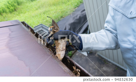 A worker cleaning garbage (dead leaves) accumulated in rain gutters A worker cleaning garbage (dead leaves) accumulated in rain gutters 94832630