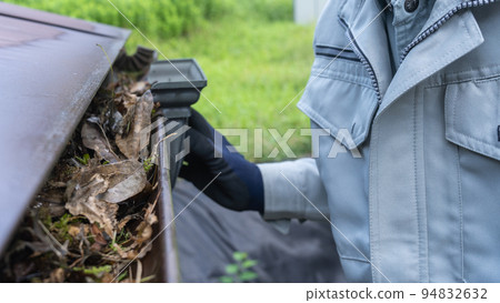 A worker cleaning garbage (dead leaves) accumulated in rain gutters 94832632