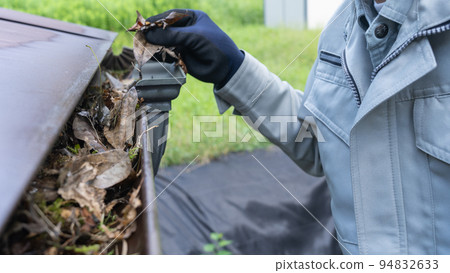 A worker cleaning garbage (dead leaves) accumulated in rain gutters 94832633