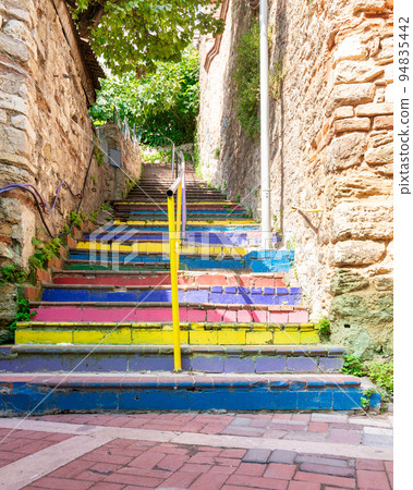 Walkway with colorful stairs between stone walls leading to ancient traditional buildings in sunny day 94835442