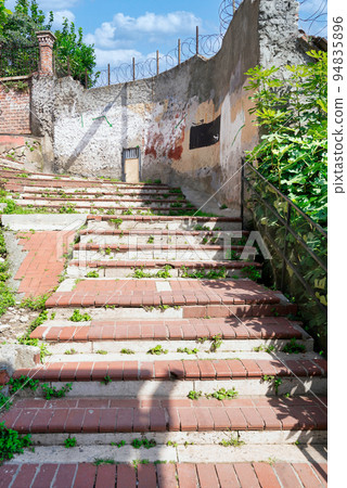 Walkway with red bricks and green trees leading to ancient traditional buildings in sunny day, Balat district, Istanbul 94835896