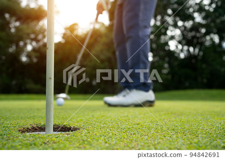 Golfer putting ball on the green golf, lens flare on sun set evening time. Golfer putting ball on the green golf, lens flare on sun set evening time. 94842691