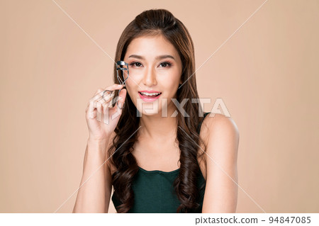 Young ardent female model with flawless beautiful skin using eyelash curler. 94847085