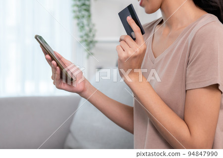 Contented young woman eagerly makes an online purchase using her smartphone. Contented young woman eagerly makes an online purchase using her smartphone. 94847990