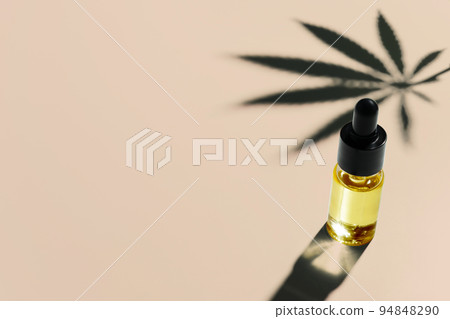 Legalized cannabis sativa hemp leaf and container of CBD oil with dropper lid. 94848290
