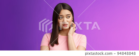 Insecure anxious young timid asian girl feel nervous scared, scratch neck worried, look sideways alarmed, feel danger, standing upset purple background distressed suffer discomfort 94848848