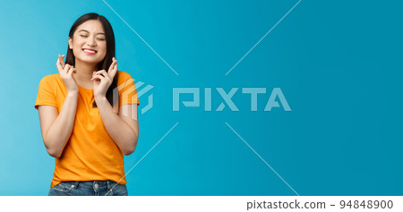 Hopeful excited asian young girl making wish cross fingers good luck, close eyes smiling believe dream come true, anticipating important event, praying good fortune, stand blue background Hopeful excited asian young girl making wish cross fingers good luck, close eyes smiling believe dream come true, anticipating important event, praying good fortune, stand blue background 94848900