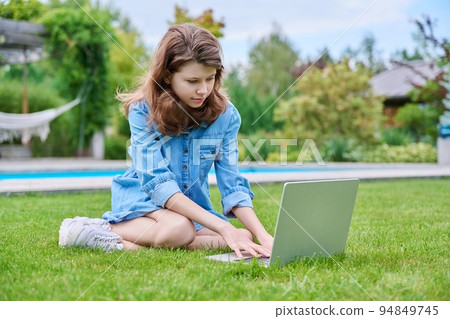Preteen girl sitting on backyard lawn using laptop for leisure and study Preteen girl sitting on backyard lawn using laptop for leisure and study 94849745