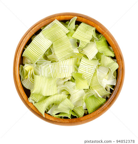 Dehydrated leek flakes, from above, in a wooden bowl. Dried strips of Allium porrum, a slightly green, crunchy and firm vegetable, with aromatic, mild and onion-like taste. Isolated, macro food photo. 94852378