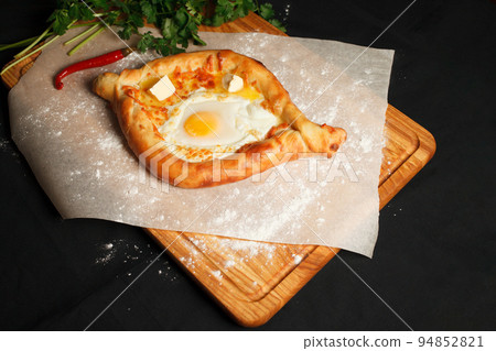 Traditional Georgian dish khachapuri ajarian in the black background. Freshly Baked Khachapuri. National Georgian pastries with cheese and raw eggs Traditional Georgian dish khachapuri ajarian in the black background. Freshly Baked Khachapuri. National Georgian pastries with cheese and raw eggs 94852821