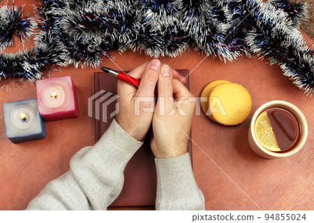 hand with pen on the office Desk festive with tea and candles 94855024