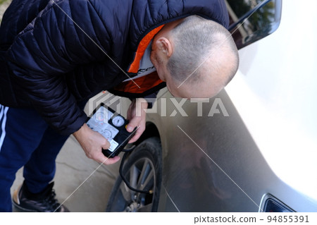 man inflating car tire with portable air compressor on street 94855391