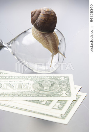 snail crawls on an hourglass against the background of money. snail crawls on an hourglass against the background of money. 94856540