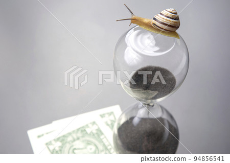 snail crawls on an hourglass against the background of money. 94856541