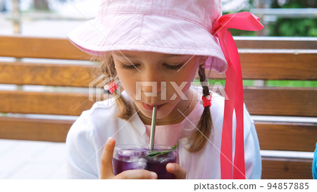 Close-up of cute little girl drinking refreshing lavender lemonade from straw in outdoor restaurant Close-up of cute little girl drinking refreshing lavender lemonade from straw in outdoor restaurant 94857885