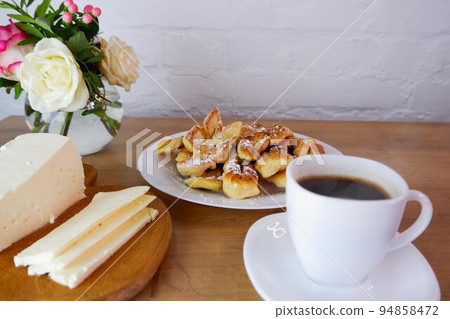 Home-baked brushwood during quarantine. Homemade dessert preparation. Simple food. Homemade feta cheese, a cup of coffee on a wooden table top. Concept on the background of a white brick wall and a Home-baked brushwood during quarantine. Homemade dessert preparation. Simple food. Homemade feta cheese, a cup of coffee on a wooden table top. Concept on the background of a white brick wall and a 94858472