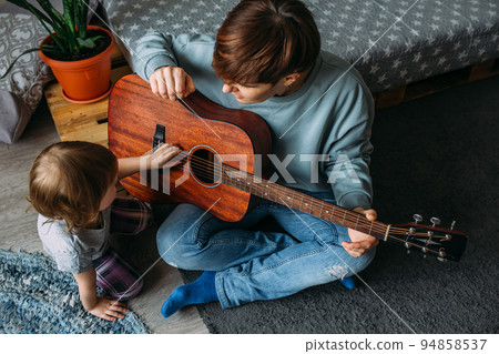 Little girl plays the guitar with her mother on the floor at home Little girl plays the guitar with her mother on the floor at home 94858537