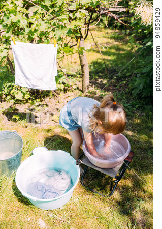 Little preschool girl helps with laundry. Child washes clothes in garden Little preschool girl helps with laundry. Child washes clothes in garden 94859429