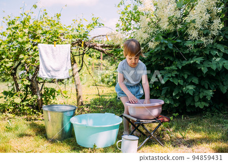Little preschool girl helps with laundry. Child washes clothes in garden 94859431