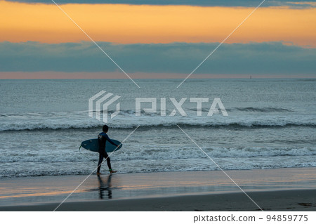 Surfer walking on the beach early in the morning Surfer walking on the beach early in the morning 94859775