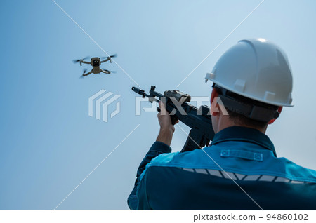 Caucasian man in a helmet shoots a flying drone with a rifle.  94860102
