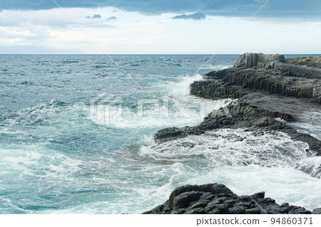 rocky seashore formed by columnar basalt against the backdrop of a stormy sea, coastal landscape of the Kuril Islands 94860371