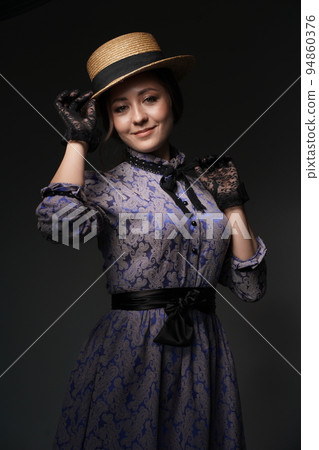 A girl in a blue retro dress in the style of the 1900s. A woman adjusts her hat in lace gloves. Historical fashion of the 19th century. High quality photo 94860376
