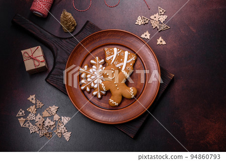 Beautiful gingerbread on a brown ceramic plate with Christmas tree decorations on a dark concrete background 94860793