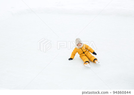 The child was skating on an ice rink and fell laughing merrily. Learn to skate. A child rides on the frozen ice of a lake outdoors. Winter sports and outdoor games. Copy space 94860844