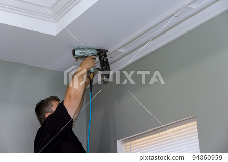 During the construction of a new house, a professional handyman nail wooden cornices to a curtain wall over the window. During the construction of a new house, a professional handyman nail wooden cornices to a curtain wall over the window. 94860959