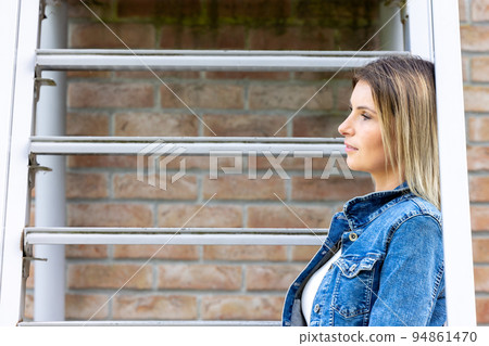 Stylish brunette girl wearing jeans vest, white t-shirt and yellow jeans posing against stairs in 94861470