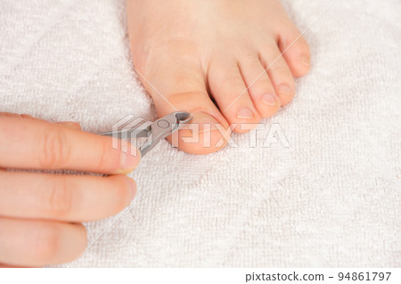A woman does a pedicure in a beauty salon, removes the cuticle from the big toe with forceps A woman does a pedicure in a beauty salon, removes the cuticle from the big toe with forceps 94861797