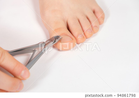 A woman does a pedicure in a beauty salon, removes the cuticle from the big toe with forceps A woman does a pedicure in a beauty salon, removes the cuticle from the big toe with forceps 94861798