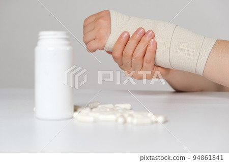 A person's hand with an elastic bandage and a jar of calcium or chondroitin tablets. Treatment of fractures, sprains and joint diseases 94861841