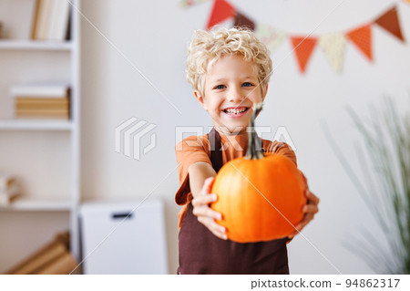Smiling kid boy laughs and holding pumpkin with during Halloween celebration Smiling kid boy laughs and holding pumpkin with during Halloween celebration 94862317