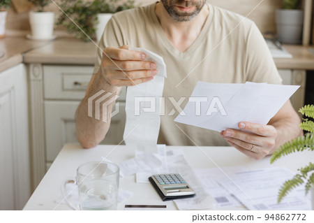 man pays bills and utilities, counts the amount of expenses and income on the calculator. Financial literacy and mortgage or rental payment man pays bills and utilities, counts the amount of expenses and income on the calculator. Financial literacy and mortgage or rental payment 94862772