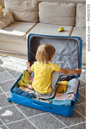 A sad child in a suitcase is waiting for departure. Family relocation, flight from the country 94863038