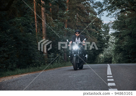 Blurred Motion A young man biker in a helmet quickly rides at high speed on a forest road, in motion Blurred Motion A young man biker in a helmet quickly rides at high speed on a forest road, in motion 94863101