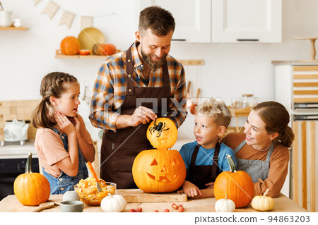 Happy family mother, father and kids to remove pulp from from pumpkin while carving jack o lantern with family 94863203