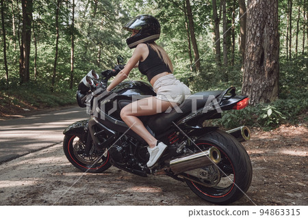 Young woman biker in a helmet sitting on a motorcycle in the underground parking garage 94863315